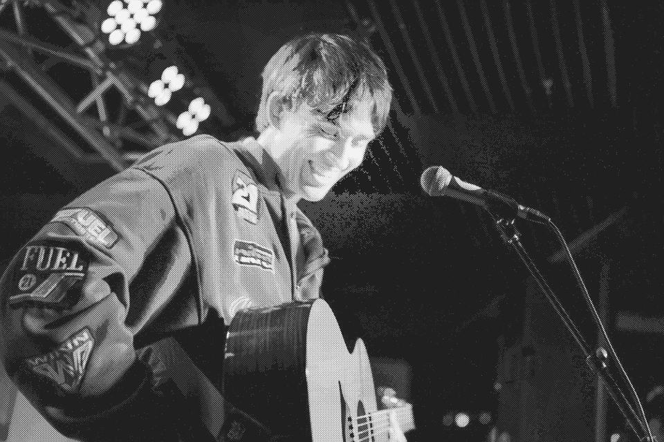 Jake Cornell smiling on stage with an acoustic guitar